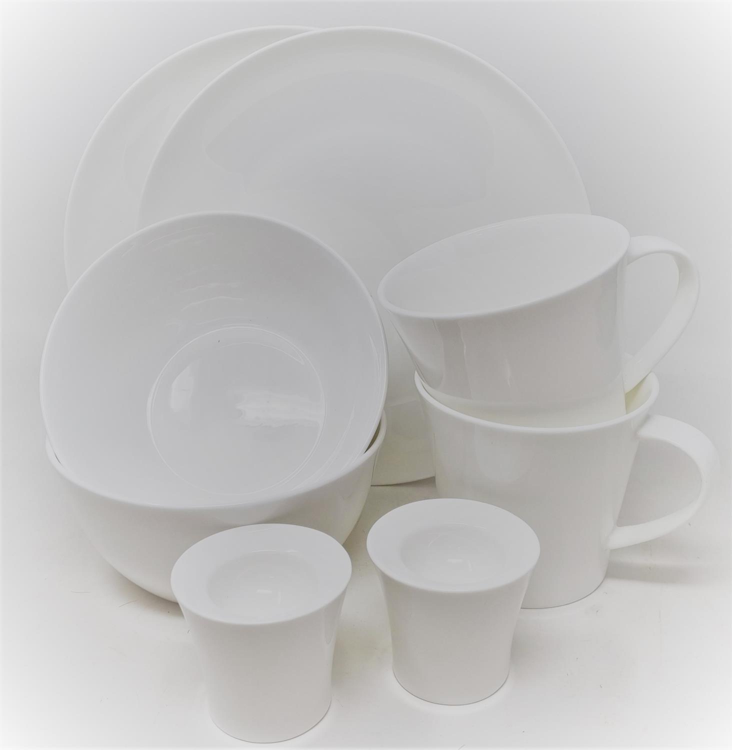 Eine Anordnung von weißen Geschirrteilen: zwei flache Teller, eine Schüssel, drei Tassen und zwei kleine Becher.