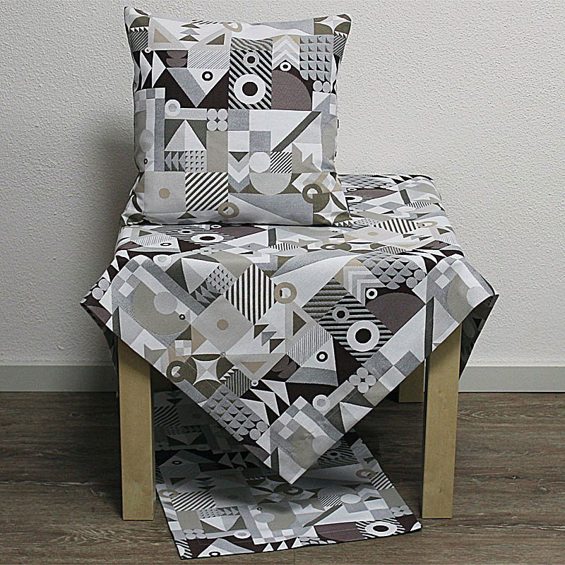 Ein Tisch mit einem geometrisch gemusterten Tischläufer und einem passenden Kissen auf einem Stuhl. Hintergrund in neutralem Farbton.