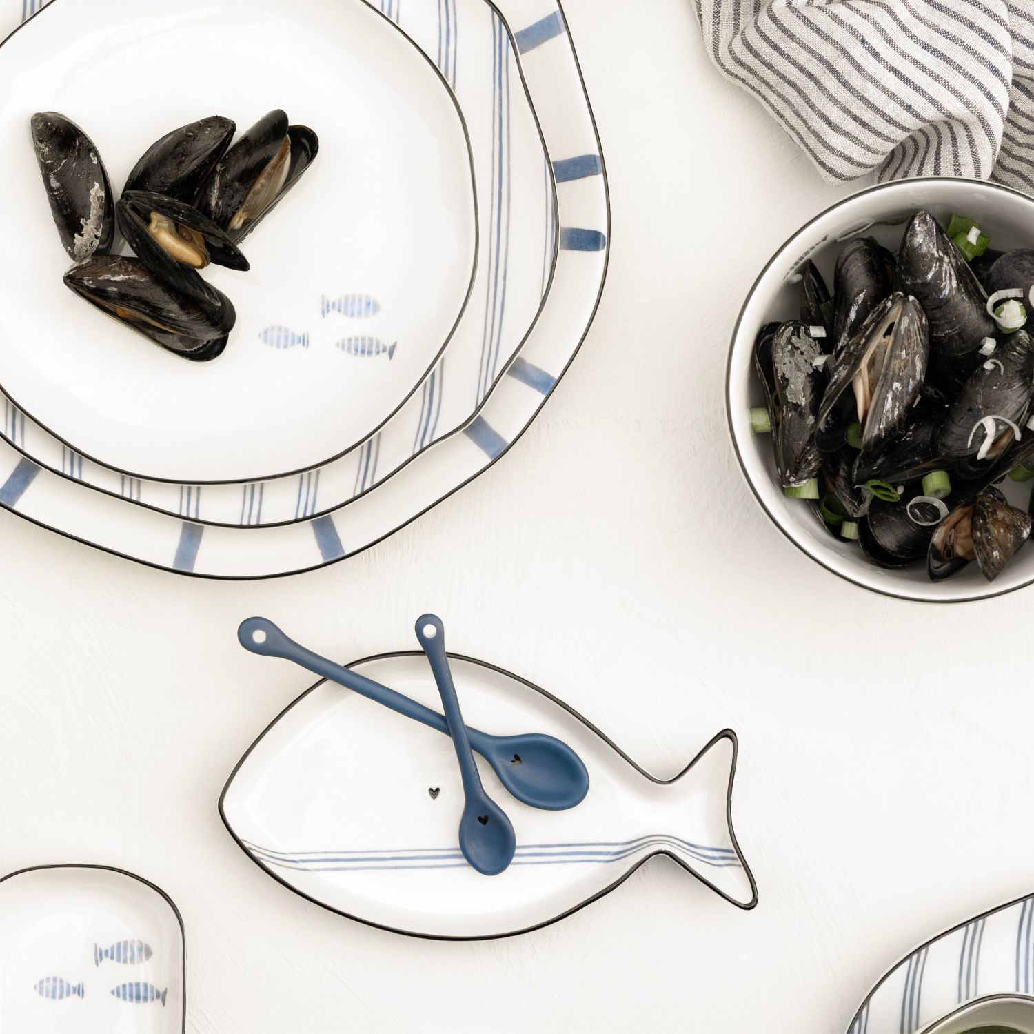 Tischszene mit Muscheln, gestreiftem Geschirr und fischförmiger Schale mit zwei blauen Löffeln